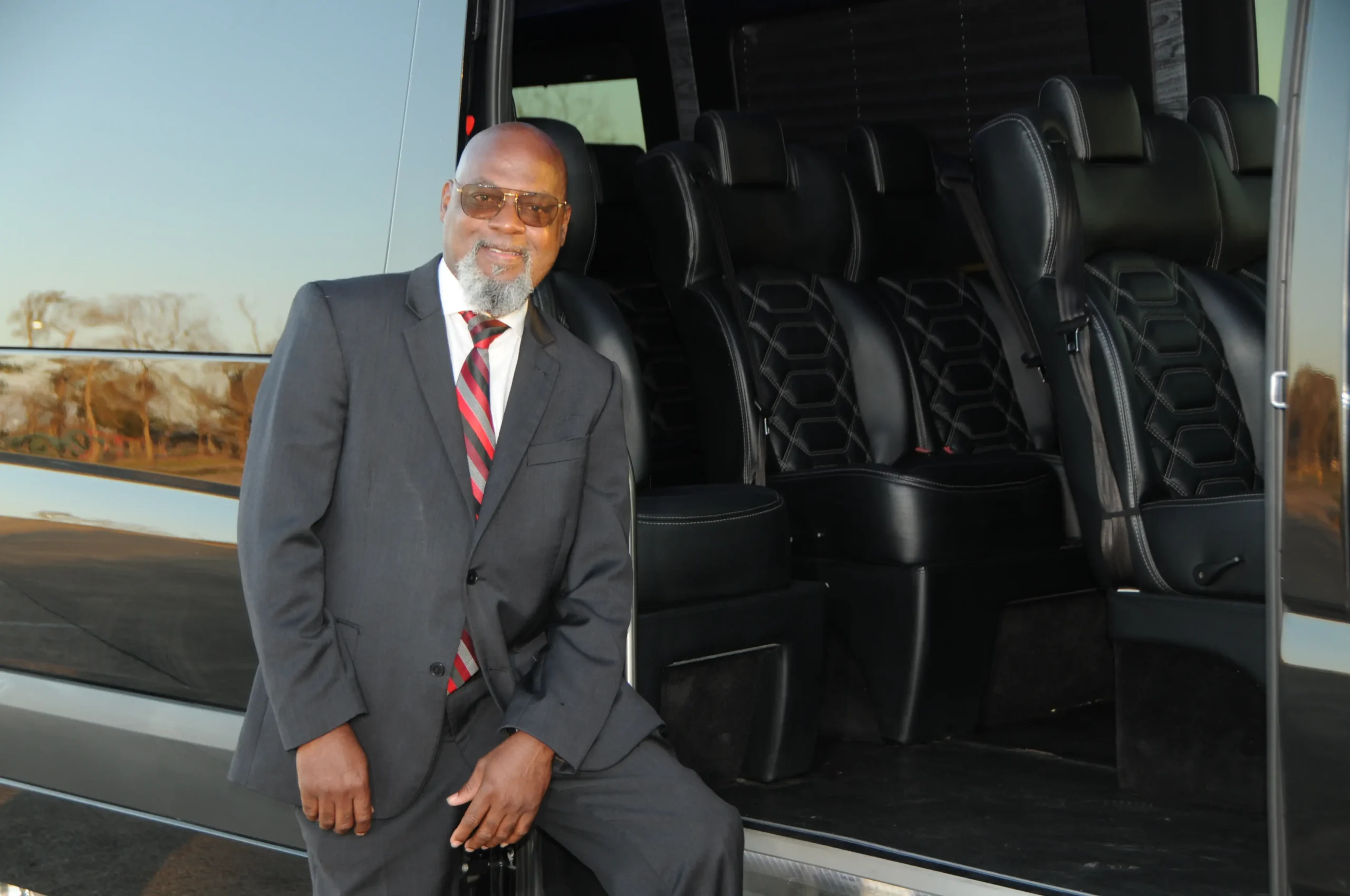 Suited Sugarland XPRS chauffeur beside a black Sprinter with passenger seating